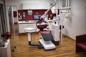 Start eine moderne zahnarztpraxis mit kastanienbraunem und weißem zahnarztstuhl, zahnärztlicher ausrüstung, schränken, einem computer und medizinischen hilfsmitteln in regalen, alles auf einem holzboden.