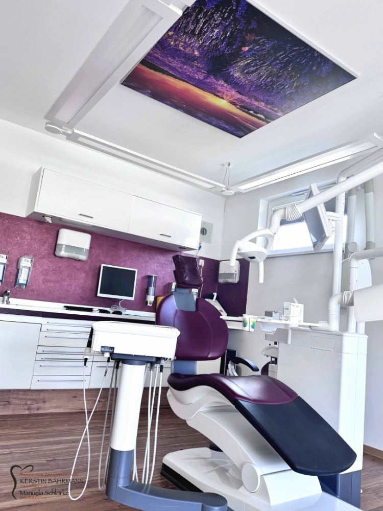 eine moderne zahnarztpraxis mit einem lilafarbenen behandlungsstuhl, weißen schränken, zahnmedizinischen geräten und einer landschaftsdarstellung an der decke. die wände sind lila und weiß, und der raum ist sauber und hell beleuchtet.
